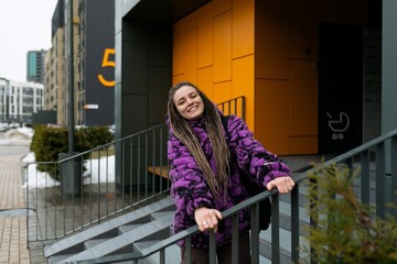 Lifestyle concept. A young woman with dreadlocks and piercings stands at the entrance to an orange...