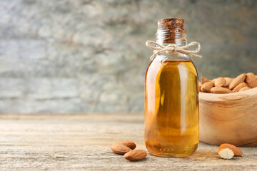 Almond oil in bottle and nuts on wooden table, closeup. Space for text