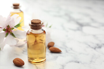 Almond oil in bottle, flower and nuts on white marble table, closeup. Space for text