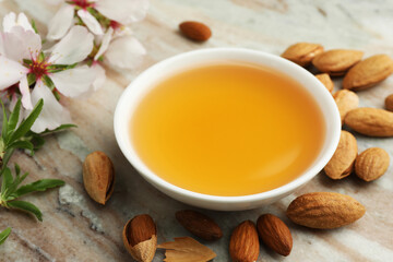 Almond oil in bowl, branch with flowers and nuts on color marble table, closeup