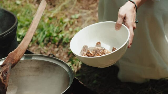 Woman with a spoon mixes empty shells from garden snails in a saucepan, which are cooked for cleaning in boiling water. The process of cooking a gourmet dish. French cuisine. Close-up. 
