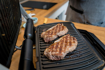 Chef at the kitchen preparing beef steaks on the home electric grill