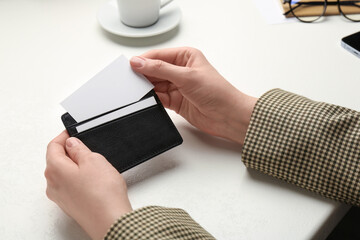 Woman holding leather business card holder with blank card at white table, closeup
