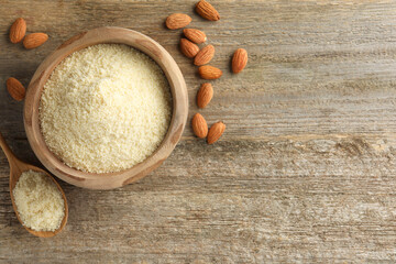 Fresh almond flour in bowl, spoon and nuts on wooden table, flat lay. Space for text