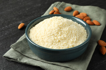 Fresh almond flour in bowl on dark textured table, closeup