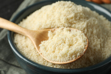 Fresh almond flour in bowl and spoon on table, closeup