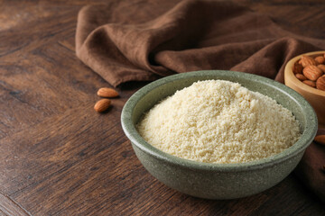 Fresh almond flour in bowl and nuts on wooden table, closeup. Space for text