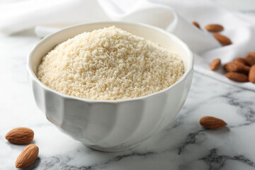 Fresh almond flour in bowl and nuts on white marble table, closeup