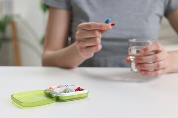 Woman with pills, organizer and glass of water at white table, selective focus