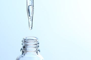 Dripping liquid from pipette into glass bottle on light blue background, closeup. Space for text