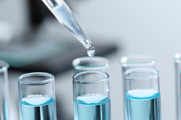 Dripping liquid from pipette into test tube on blurred background, closeup