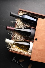 Box with wine bottles, corkscrew and corks on dark textured table, flat lay