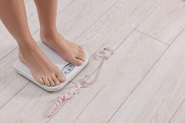 Woman standing on floor scale and measuring tape at home, closeup. Space for text