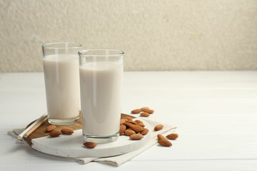 Glasses of almond milk and almonds on white wooden table, space for text