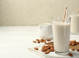 Glasses of almond milk and almonds on white wooden table, space for text