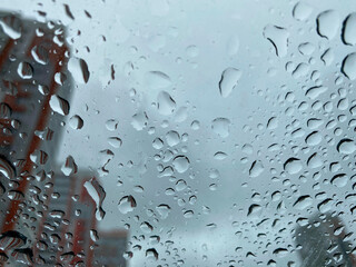 raindrops on the glass through which you can see the cloudy sky and multi-storey buildings
