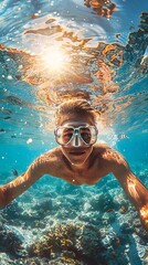 A man wearing a snorkeling mask takes a selfie underwater. The background shows the sun's rays breaking through the surface of the water.