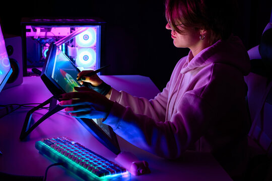 Female designer works on a Drawing tablet with Screen. A woman in a room with neon lighting draws with a stylus on a graphics tablet. 3D artist is working on a project