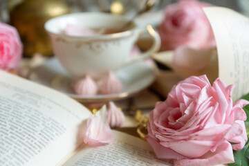 A cup of aromatic tea, a book and a rose on the table.