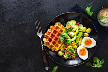 Healthy breakfast or brunch featuring boiled eggs, salad with avocado, olives and cheese waffles on a white marble background with copy space top view