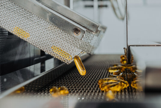 Capsule production. Yellow transparent capsules with oil moving down a conveyor belt. Pharmaceutical manufacturing. Dietary supplement factory. Omega, vitamins D, E. Close-up of a capsule.