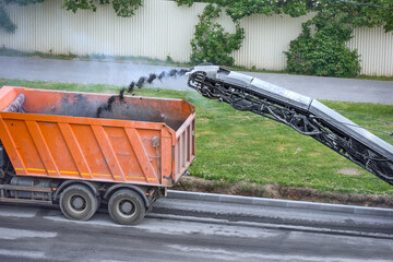 The asphalt cut from the road is poured along a conveyor into the body of a dump truck. Men at work.