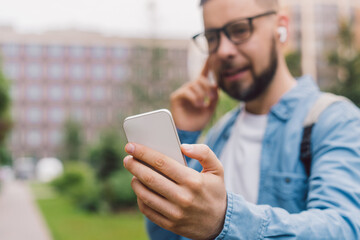 Close up cropped shot of a youn casually dressed business man having video call outdoors using wireless earphones and smartphone