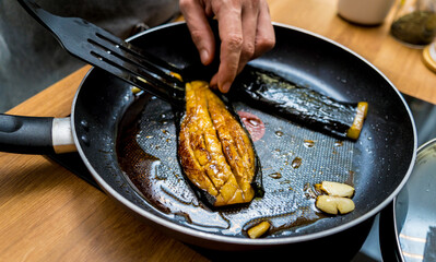 Chef at the kitchen preparing grilled eggplants with garlic