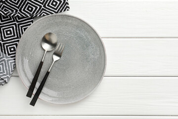 Stylish setting with cutlery, napkin and plate on white wooden table, top view. Space for text