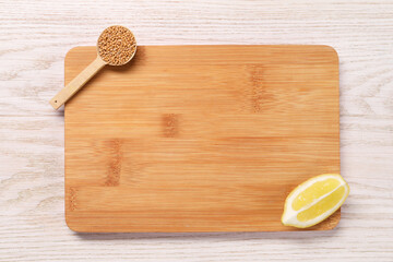 Cutting board, dry mustard and lemon on light wooden table, top view. Space for text