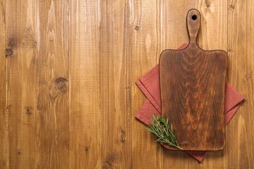 Cutting board, rosemary and napkin on wooden table, top view. Space for text