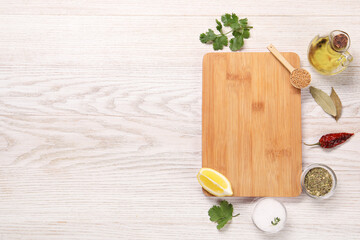 Cutting board, spices, oil and lemon on light wooden table, flat lay. Space for text