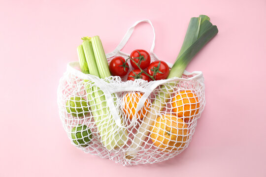 String bag with different vegetables and fruits on pink background, top view