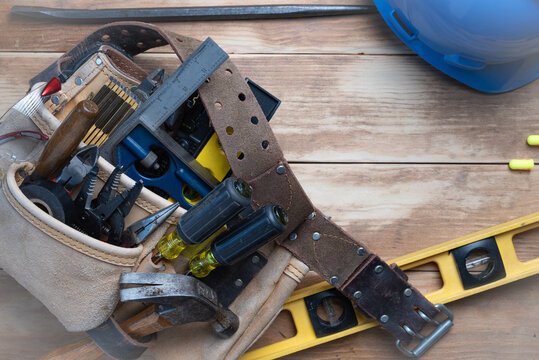 Labor Day Background with toolbelt, various hand tools, level, prybar, and protective equipment on wooden background.