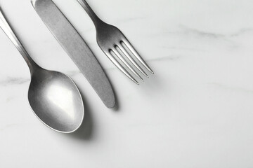 Stylish silver cutlery set on white marble table, flat lay. Space for text