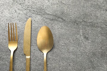 Stylish golden cutlery on grey table, flat lay. Space for text