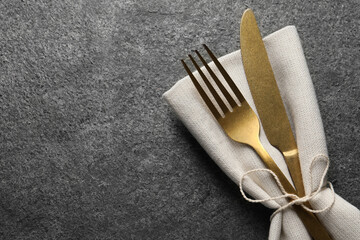 Stylish golden cutlery and napkin on grey table, top view. Space for text