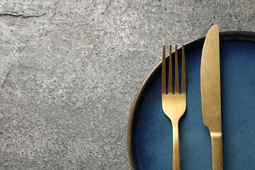 Stylish golden cutlery and plate on grey table, top view. Space for text