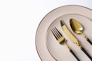 Stylish golden cutlery and plates on white background, top view. Space for text