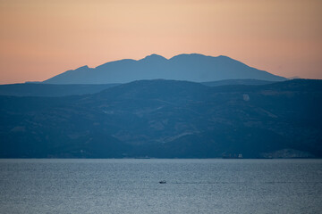 A view of the hills and mountains on the opposite shore of the sea and a boat sailing in the distance at dusk
