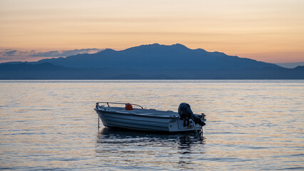 A small boat floats on the sea at sunset