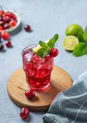 Cherry-lime mojito cocktail with mint, lime and ice on a wooden board on a blue background with fresh berries and napkin.