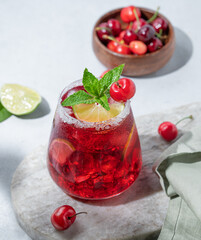 Cherry-lime mojito cocktail with mint, lime and ice on a marble  board on a light background with napkin and shadow close up.