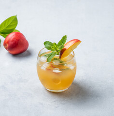 Refreshing peach cocktail, lemonade or iced tea in a glass on a light background.