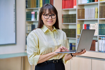 Middle aged elegant woman using laptop inside library