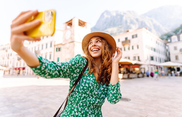 Pretty woman walks the streets and takes selfie using smartphone camera.  Travel, blogging, weekend, relax and lifestyle concept.