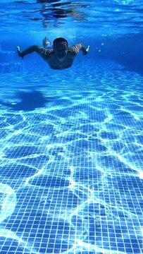 Man swimming under water in the pool. Underwater view of a male swimmer floating in transparent water to the camera. Vertical video