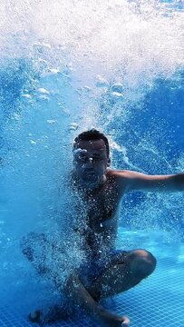 Man jumps into clear water of a pool in yoga pose. Underwater camera shooting a video of a man jumping into water. Male shows gesture yes with thumbs underwater. Vertical video