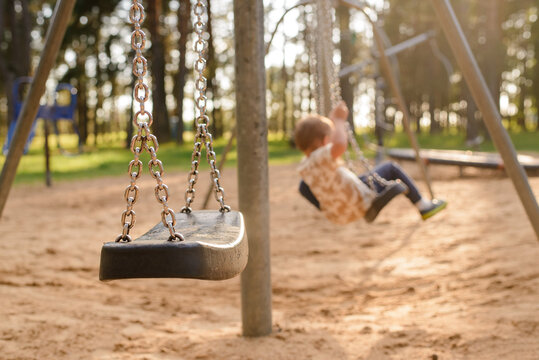 a little boy is sitting on the ground in the park, empty swing in the foreground