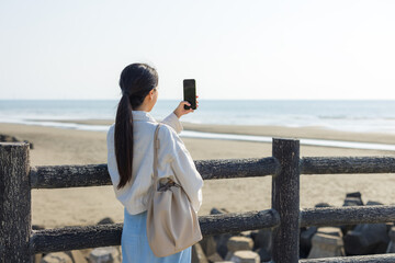 Woman use of mobile phone to take photo on the sea